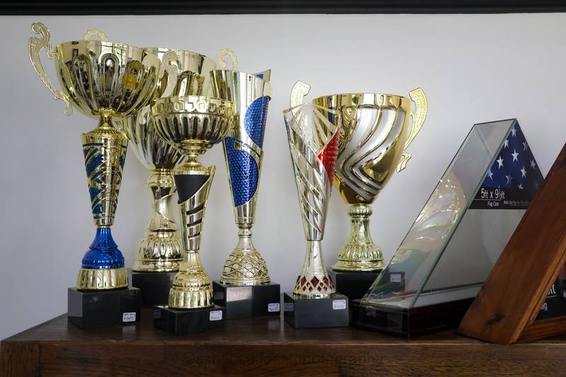 Gold and colored trophy cups beside a glass flag display case
